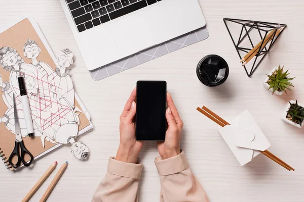 Office desk with laptop and woman hands holding smartphone with blank screen, flat lay — Stock Photo