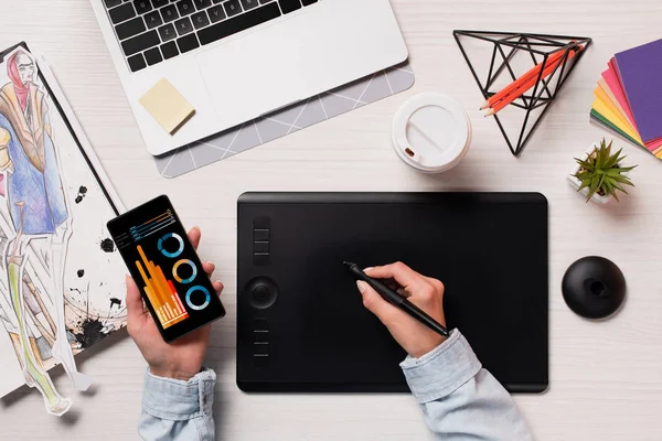 Cropped view of designer using graphics tablet, pen and smartphone with graphs on screen, flat lay — Stock Photo