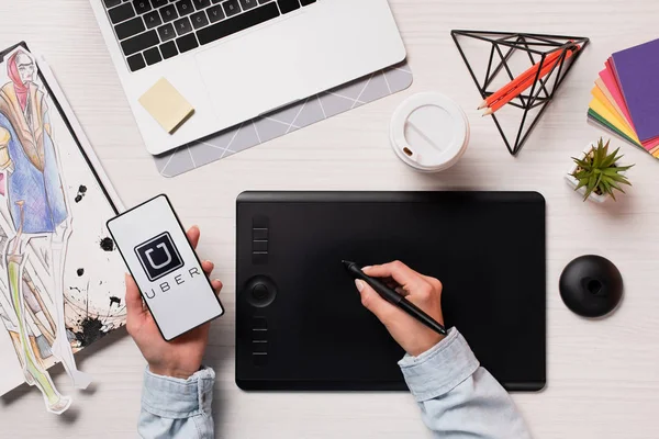 Cropped view of designer using graphics tablet, pen and smartphone with uber app on screen, flat lay — Stock Photo