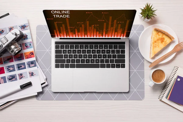 Office desk with laptop with online trading website on screen, flat lay — Stock Photo