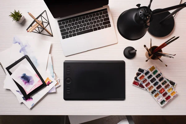 Escritorio de oficina con ordenador portátil, tabletas gráficas, bolígrafo y suministros de arte, disposición plana - foto de stock