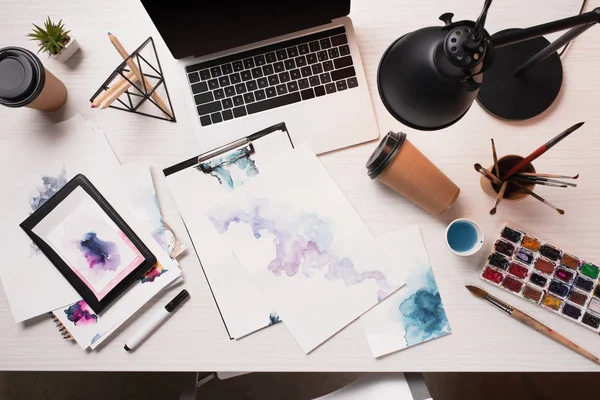 Plano de escritorio de oficina desordenado con ordenador portátil, bocetos y suministros de arte - foto de stock