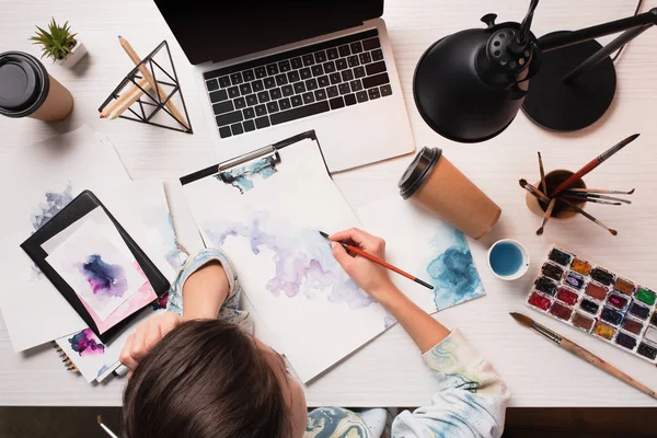 Office desk with laptop, art supplies and drawing female artist, flat lay — Stock Photo