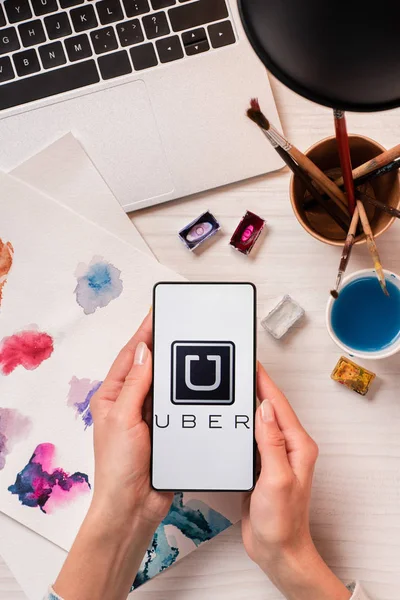 Vista cortada de designer segurando smartphone com aplicativo uber na tela, flat lay — Fotografia de Stock