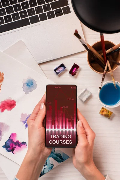 Cropped view of designer at office desk holding smartphone with graph on screen, flat lay — Stock Photo