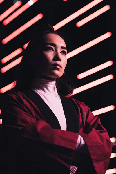 Niedrigwinkel-Ansicht attraktiver asiatisches Mädchen in weinrotem Kimono auf der Straße mit Neonlicht am Abend, Stadt der Zukunft Konzept — Stockfoto