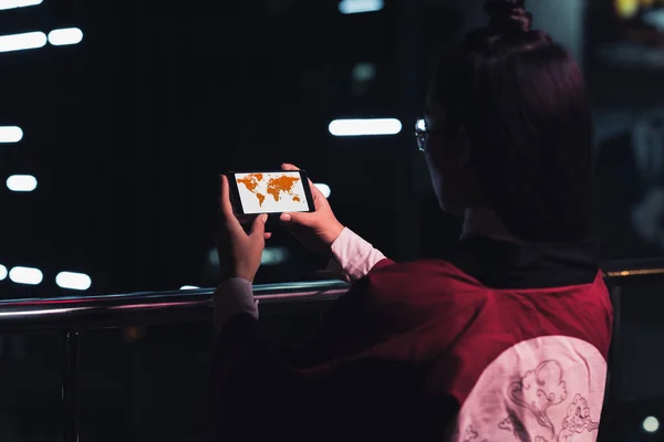 Back view of girl holding smartphone with travel appliance on street with neon light in evening, city of future concept — Stock Photo