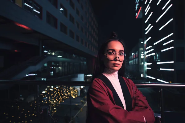 Belle asiatique fille en bordeaux kimono et lunettes regardant caméra sur rue le soir, ville du futur concept — Photo de stock