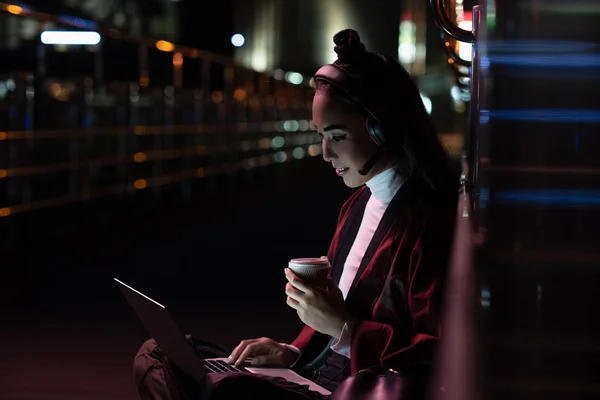 Atraente asiático menina no quimono sentado e ter vídeo chat no rua com neon luz, cidade de futuro conceito — Fotografia de Stock