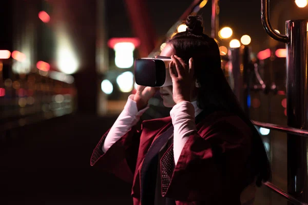 Attraente asiatico ragazza utilizzando virtuale realtà auricolare su strada in sera città del futuro concetto — Foto stock