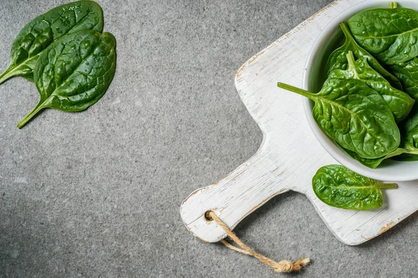 Top view of green juicy spinach leaves in bowl on white wooden cutting board — Stock Photo