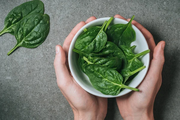 Top view of male hands holding spinach leaves in bowl — Stock Photo