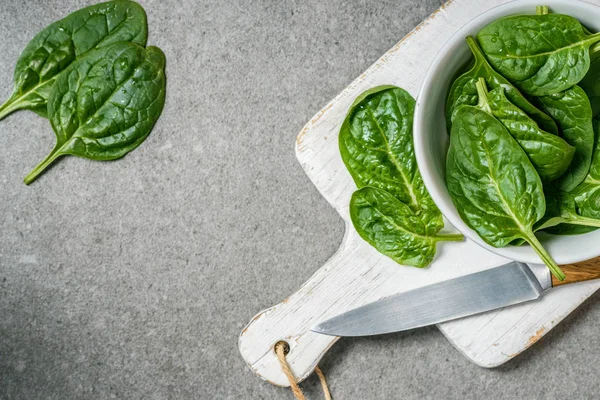 Veta superior de hojas de espinacas orgánicas y verdes en un tazón en una tabla de cortar blanca - foto de stock