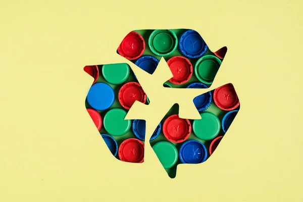 Top view of recycle sign with bottle caps pattern on yellow background — Stock Photo