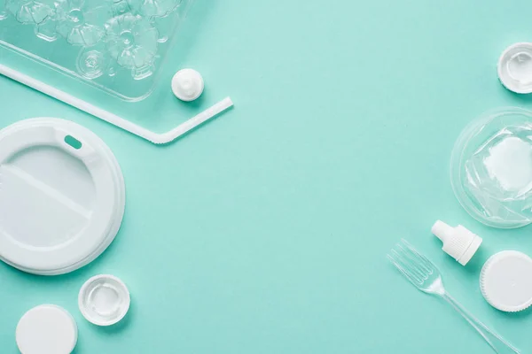 Top view of plastic bottle caps, drinking straw, fork, eggs tray and lid for drink on blue background — Stock Photo