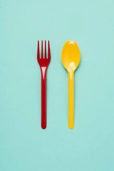 Top view of red plastic fork and yellow spoon on blue background — Stock Photo