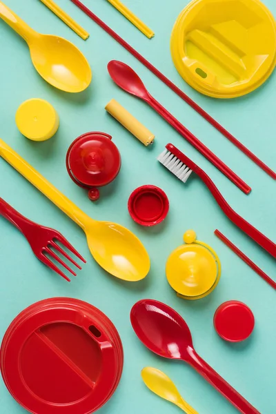 Colocación plana con artículos de plástico desechables rojos y amarillos dispuestos sobre fondo azul - foto de stock