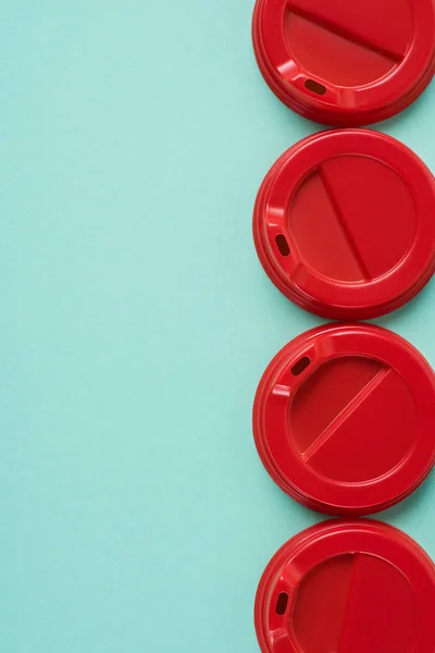 Vue du dessus de quatre couvercles jetables rouges pour boisson disposés sur fond bleu — Photo de stock