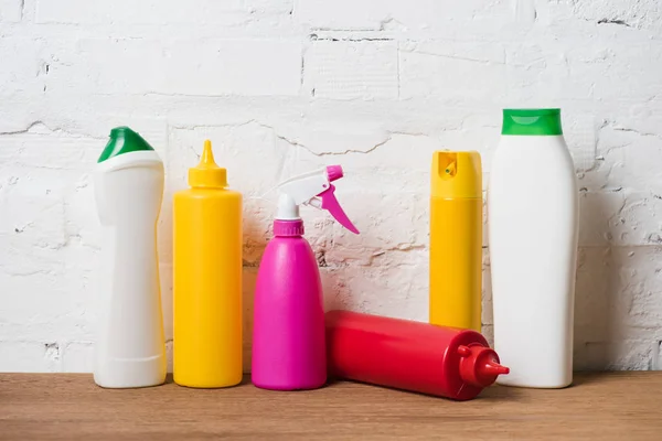 Diferentes botellas de plástico de colores en la mesa de madera sobre fondo de pared de ladrillo - foto de stock