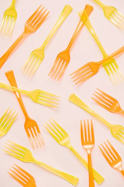 Draufsicht auf bunte orangefarbene und gelbe Plastikgabeln auf rosa Hintergrund — Stockfoto