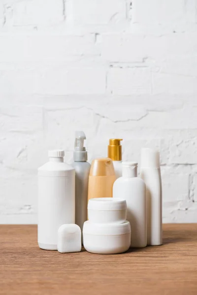 Botellas de plástico blanco y dorado sobre mesa de madera sobre fondo de pared de ladrillo - foto de stock