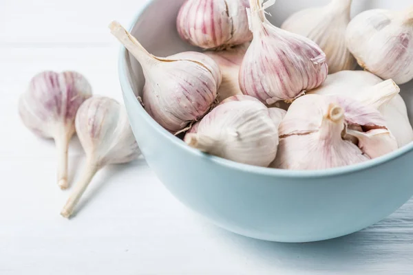 Knoblauchzwiebeln in blauer Keramikschale auf weißem Holztisch — Stockfoto