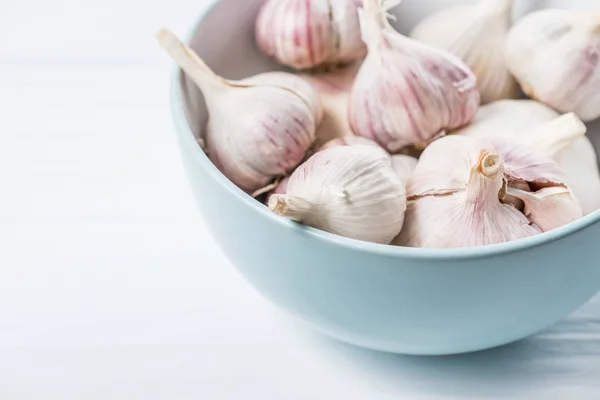 Garlic bulbs in blue ceramic bowl on white table — Stock Photo