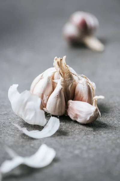 Peeled bulb of garlic with husk on grey marble table — Stock Photo