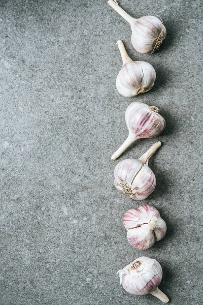 Top view of vertical row of ripe garlic bulbs on grey background — Stock Photo