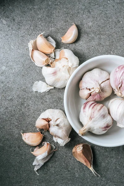 Ansicht von Knoblauch in Keramikschale und mehreren geschälten Zwiebeln auf grauem Hintergrund — Stockfoto