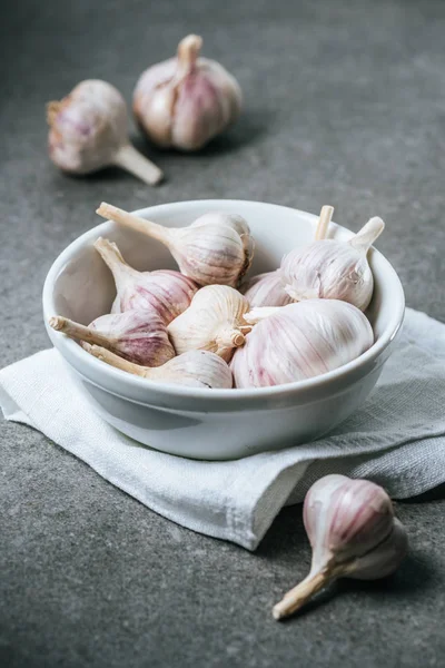 Garlic bulbs in ceramic bowl with white cloth on grey background — Stock Photo