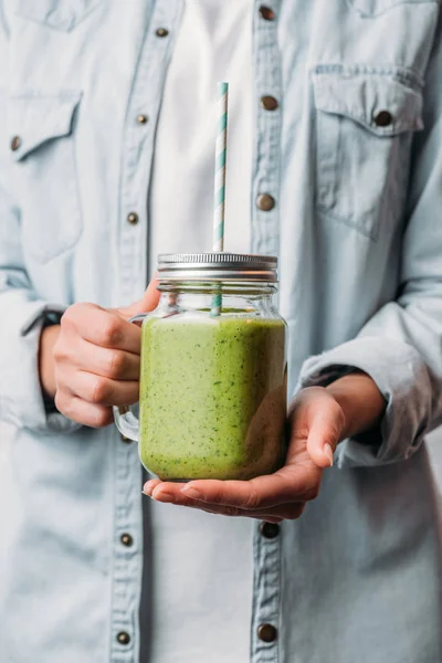 Manos femeninas sosteniendo frasco de vidrio con batido verde nutritivo y paja - foto de stock