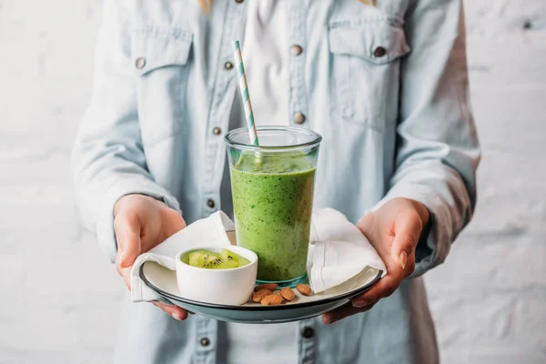 Frauenhände halten Teller mit Glas grünen Smoothie und Stroh — Stockfoto