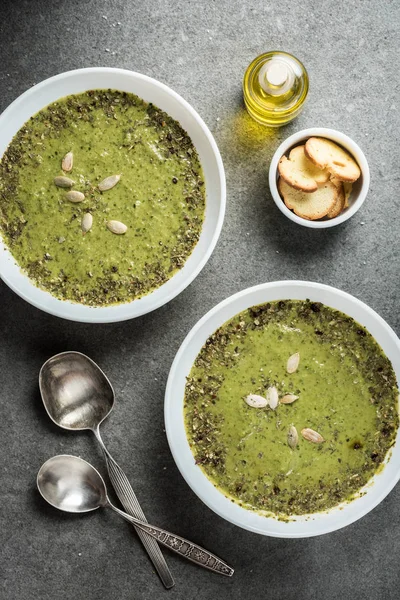 Top view of silver spoons, oil, croutons and fresh vegetable creamy soup in bowls — Stock Photo