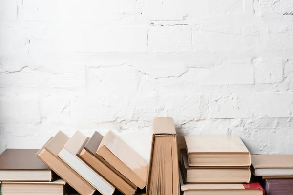 Livros com capas duras perto de parede de tijolo branco, fundo educacional — Fotografia de Stock