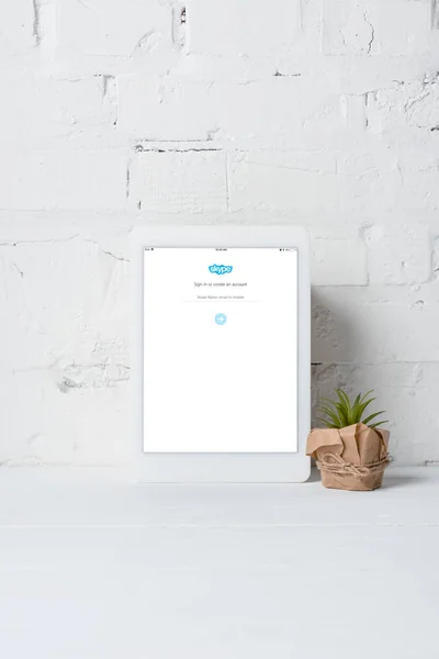 Tableta digital con aplicación skype y planta en maceta verde cerca de la pared de ladrillo blanco - foto de stock