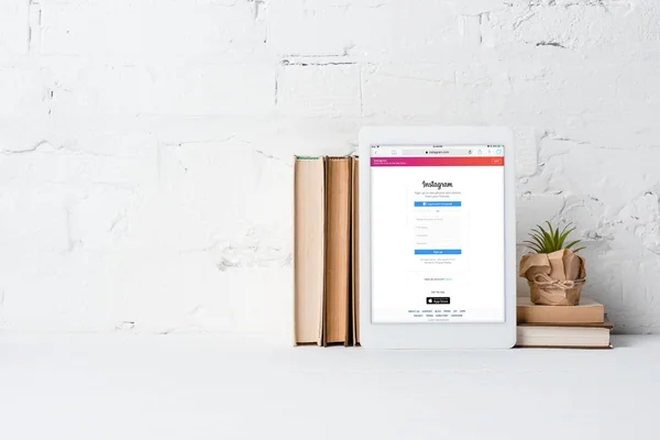 Цифровой планшет с приложением Instagram, книги и горшок завод возле стены белого кирпича — стоковое фото