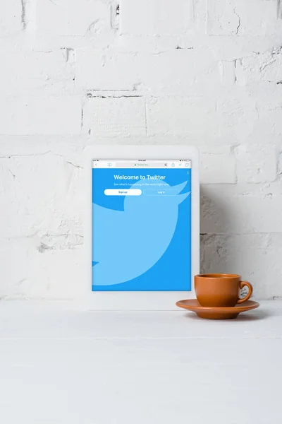 Tablet digitale con applicazione twitter e tazza di caffè vicino alla parete di mattoni bianchi — Foto stock