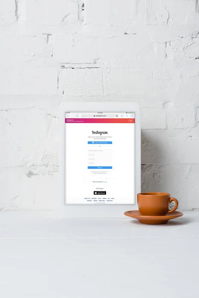 Tablet digital com aplicação instagram e xícara de café perto da parede de tijolo branco — Fotografia de Stock