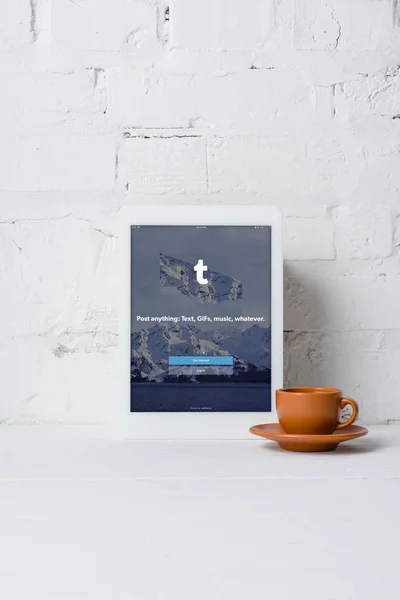 Compressa digitale con applicazione tumblr e tazza di caffè vicino alla parete di mattoni bianchi — Foto stock