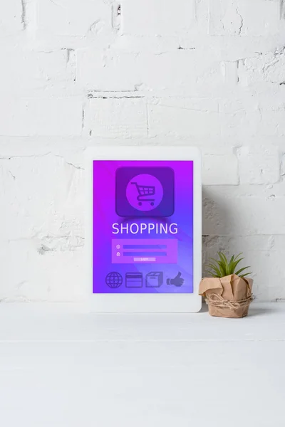Tablette numérique avec application shopping et plante verte en pot près du mur de briques blanches — Photo de stock