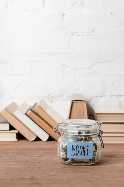 Крупним планом скляна банка з заощадженнями та книгами на дерев'яному столі — стокове фото
