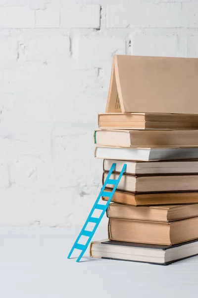 Pile of books and small blue step ladder near white brick wall — Stock Photo