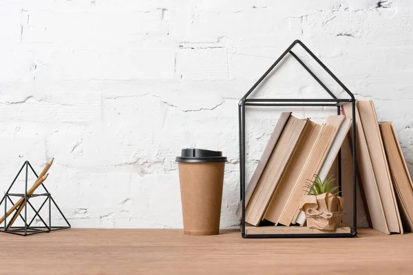 Café para llevar, planta en maceta verde y libros sobre mesa de madera - foto de stock