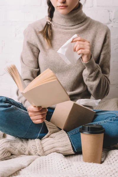 Cropped shot of woman holding paper tissue and reading book — Stock Photo