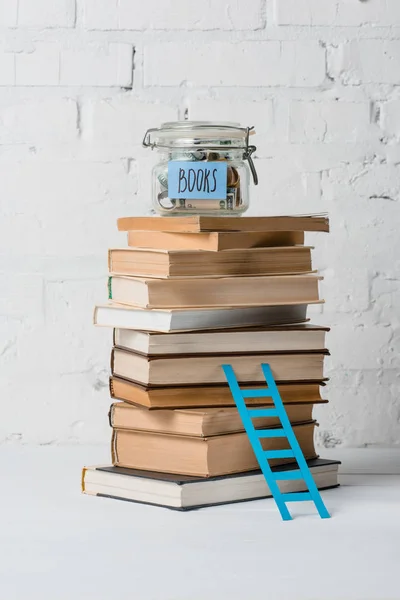 Pile de livres, petite échelle et bocal en verre avec des économies et des livres d'inscription — Photo de stock