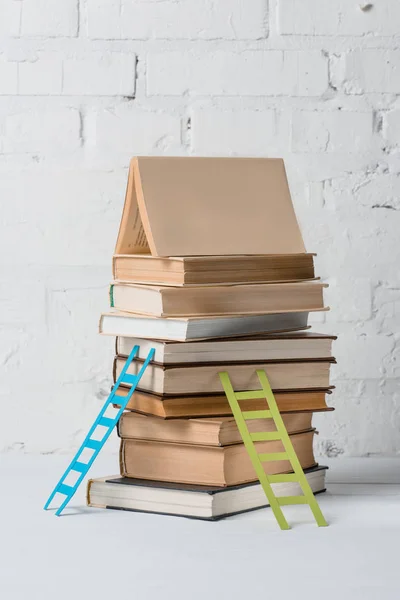 Pila de libros y escaleras de pequeño escalón cerca de la pared de ladrillo blanco - foto de stock