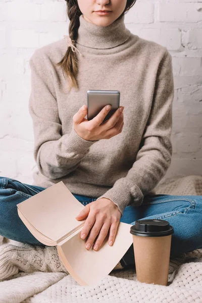 Обрезанный снимок девушки с книгой и с помощью смартфона — стоковое фото
