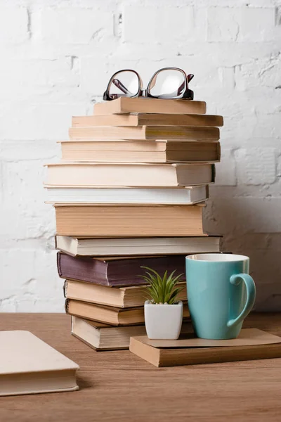 Pile of books, eyeglasses, potted plant and cup with hot beverage on wooden table — Stock Photo