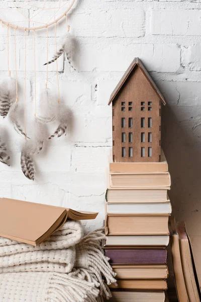 Libros, atrapasueños y casa de madera decorativa cerca de la pared de ladrillo blanco — Stock Photo